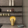 Nodo table lamp in matte gold steel, warm lighting in a contemporary kitchen setting.