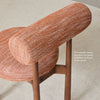 Close-up of the rich textured terracotta upholstery of the PILLO Dining Chair, with thich backrest and beautiful warm wooden legs.